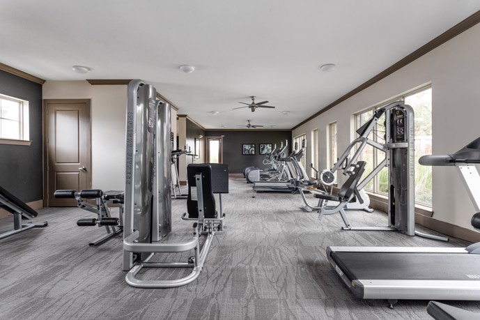 Fitness center with cardio and weight equipment, featuring ceiling fans and large windows